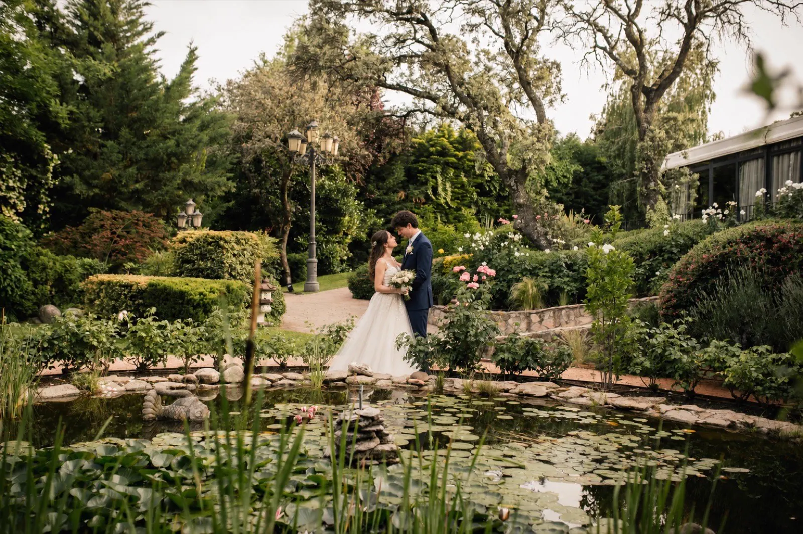 Novios besándose junto al estanque · jardín de la finca